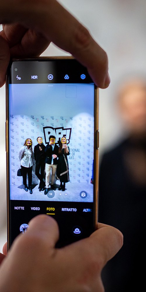Creaa Progetti: PAFF! Cellulare che scatta una foto a 4 persone davanti al manifesto di una mostra del PAFF!