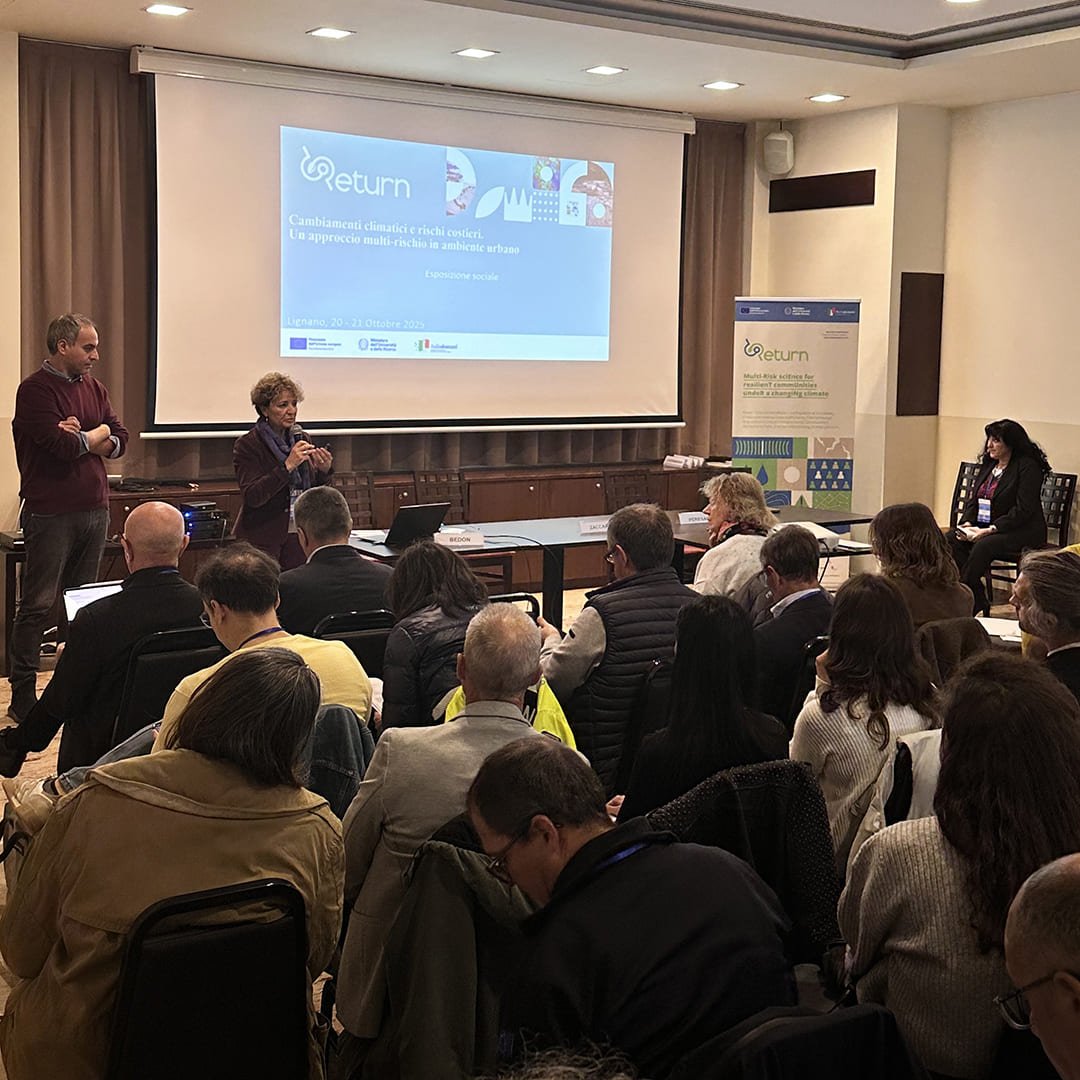 Un momento dell’evento RETURN a Lignano, con una relatrice al microfono e il pubblico attento nella sala plenaria.