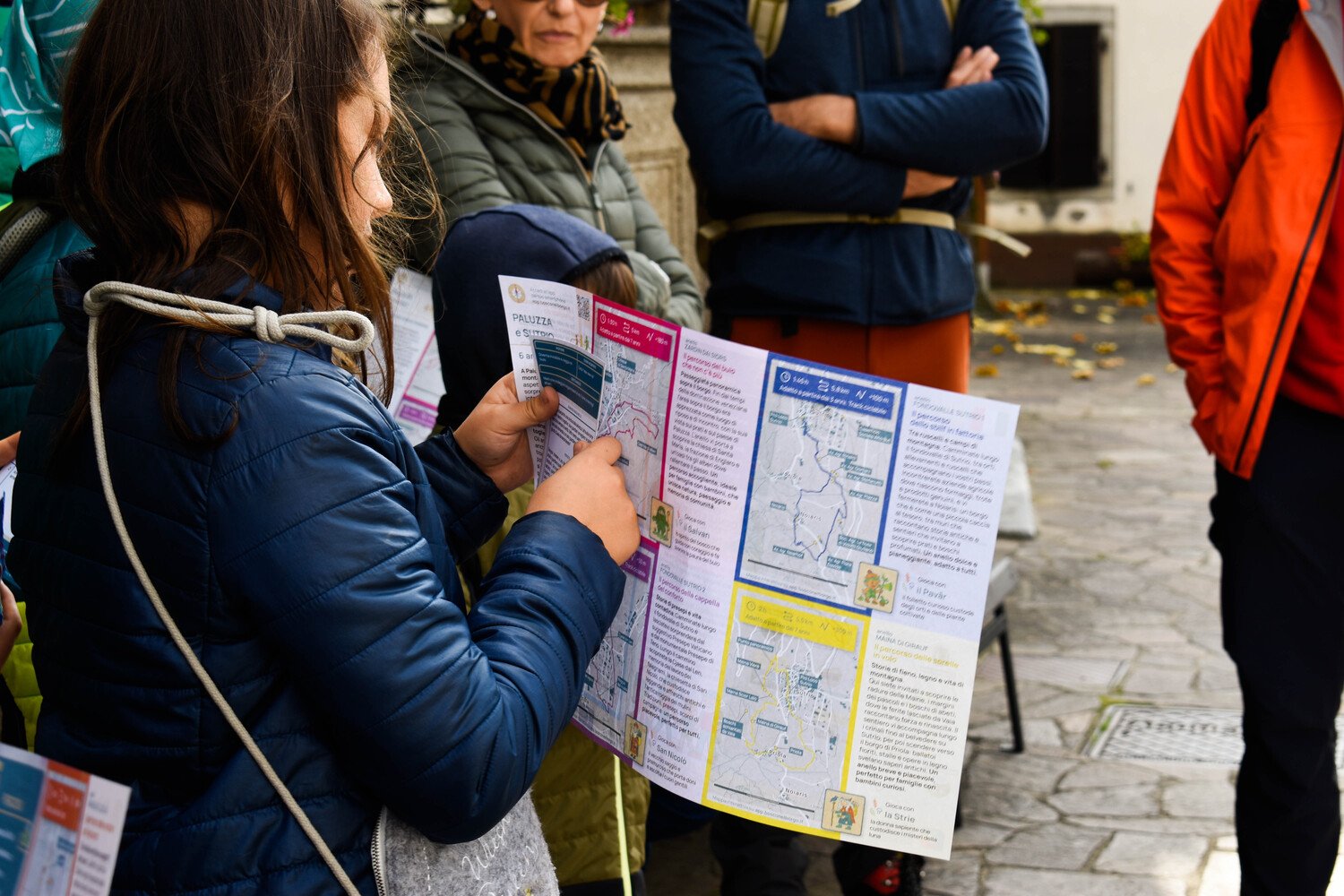 Passeggiate animate a Paluzza Bambina che consulta la mappa dei percorsi ad anello per famiglia di Paluzza e Sutrio